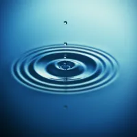 Close-up of a water droplet creating ripples on a calm, blue surface, symbolizing tranquility and mindfulness.