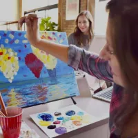 Person painting on easel with paints showing.