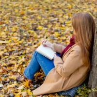 A woman sitting among the fall eaves writing.