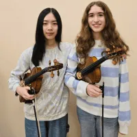 A photo of Emma Xiong (Chang) and Lily Kimble each holding a violin,
