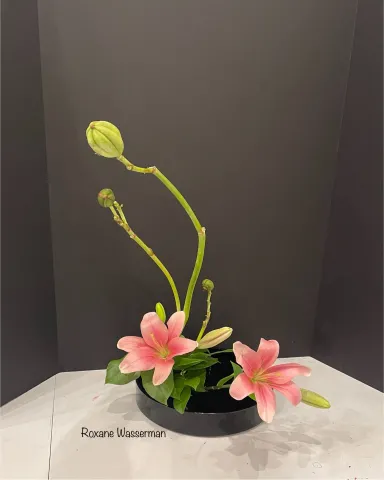 Ikebana flower arrangement - pink flowers in black vase on a table.