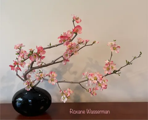 Ikebana flower arrangement - pink flowers in black vase on a table 