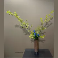 Ikebana flower arrangement - blue flowers with green leafy branches in brown vase on a table dramatically lit