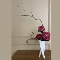 Ikebana flower arrangement - purple flowers in white vase on a table with window in background