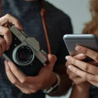 a man holding an analog camera standing next to woman holding a smart phone