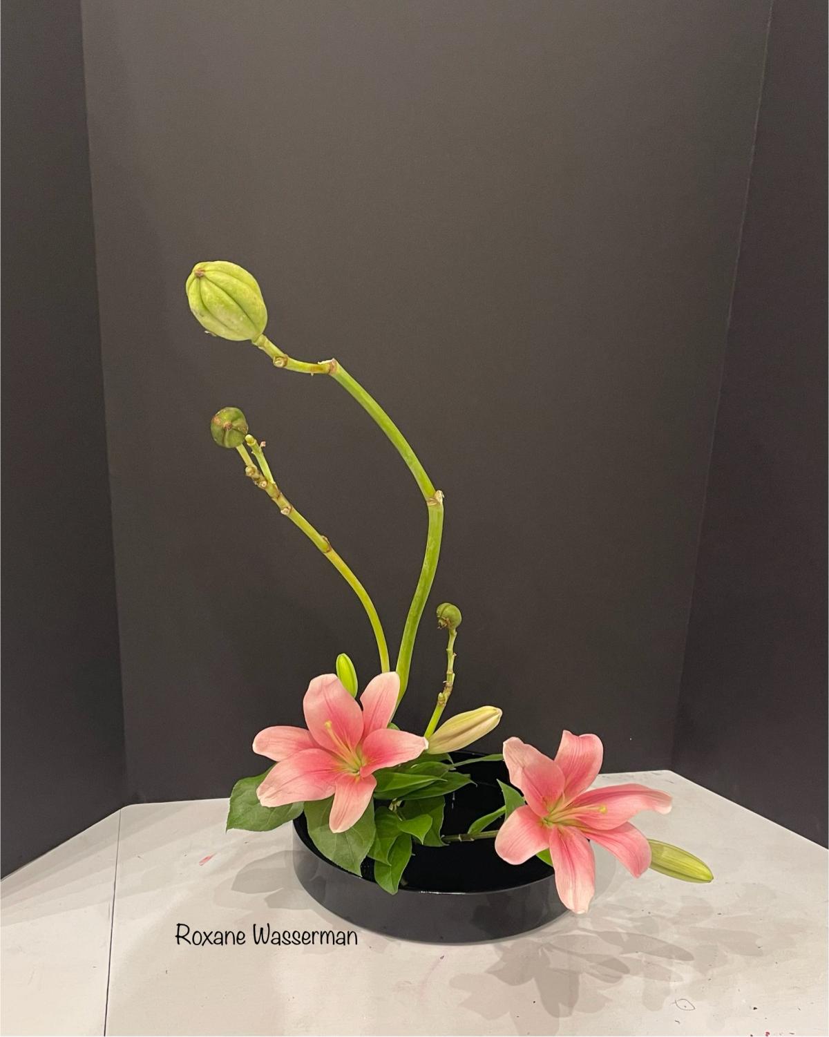 Ikebana flower arrangement - pink flowers in black vase on a table.