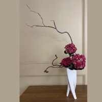 Ikebana flower arrangement - purple flowers in white vase on a table with window in background